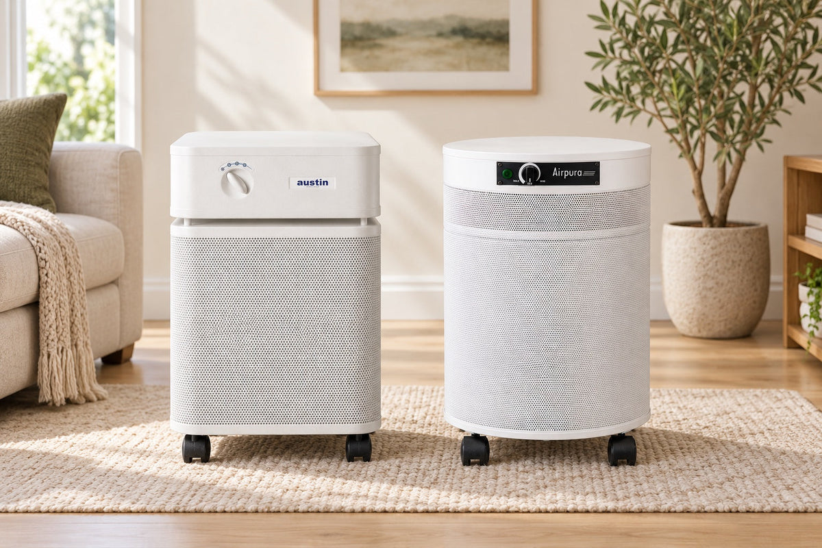 White Austin Air HealthMate and Airpura R600 air purifiers side by side on a rug in a bright living room