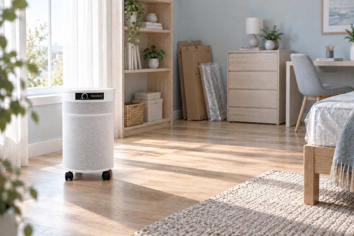 White Airpura F600 air purifier in a freshly furnished bedroom with new pressed-wood furniture, flattened cardboard boxes, and a plastic-wrapped mattress